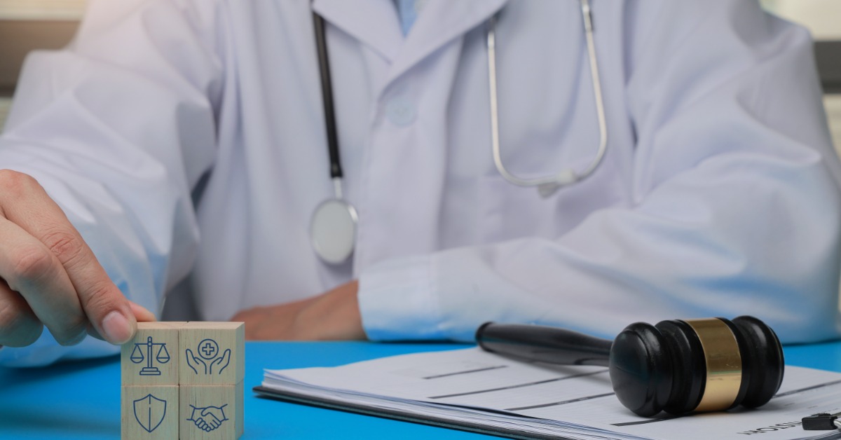 A doctor in a white coat sits behind a gavel, documents, and wooden blocks with legal and health icons.